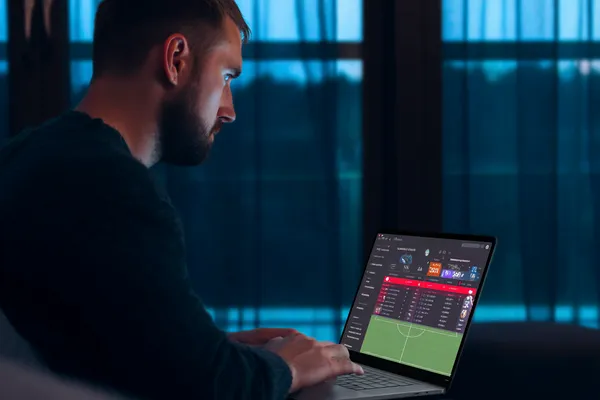 1111DB Mobile App — Your complete hub for casino and sports A man focused on his laptop with live stats in the background, highlighting the dedicated sports and gaming features of the 1111DB mobile app.